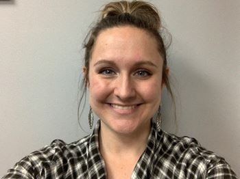 A woman with a plaid shirt and earrings smiles at the camera.